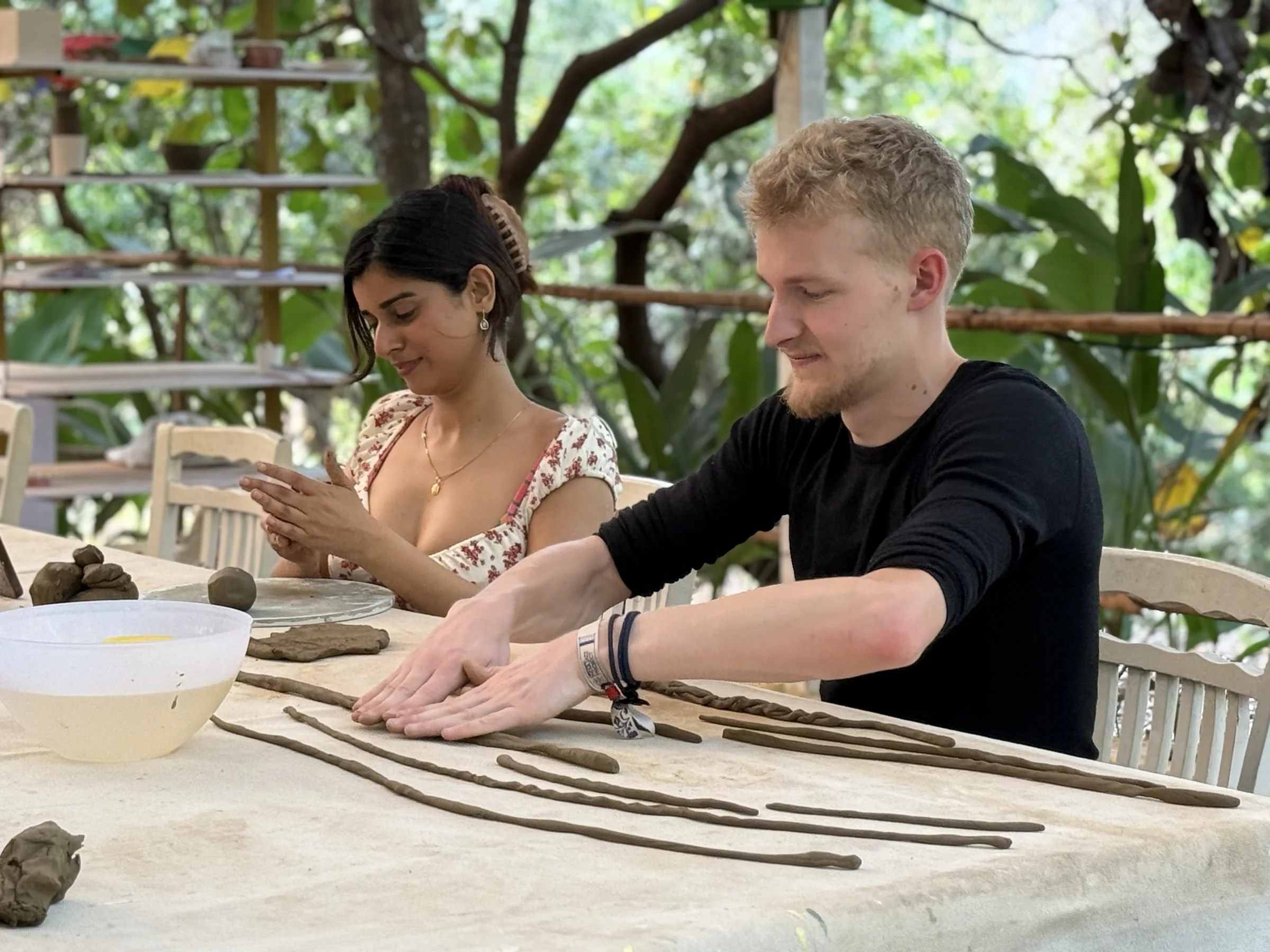 Two retreat participants rolling coils and building clay forms together at a shared worktable in Goa.