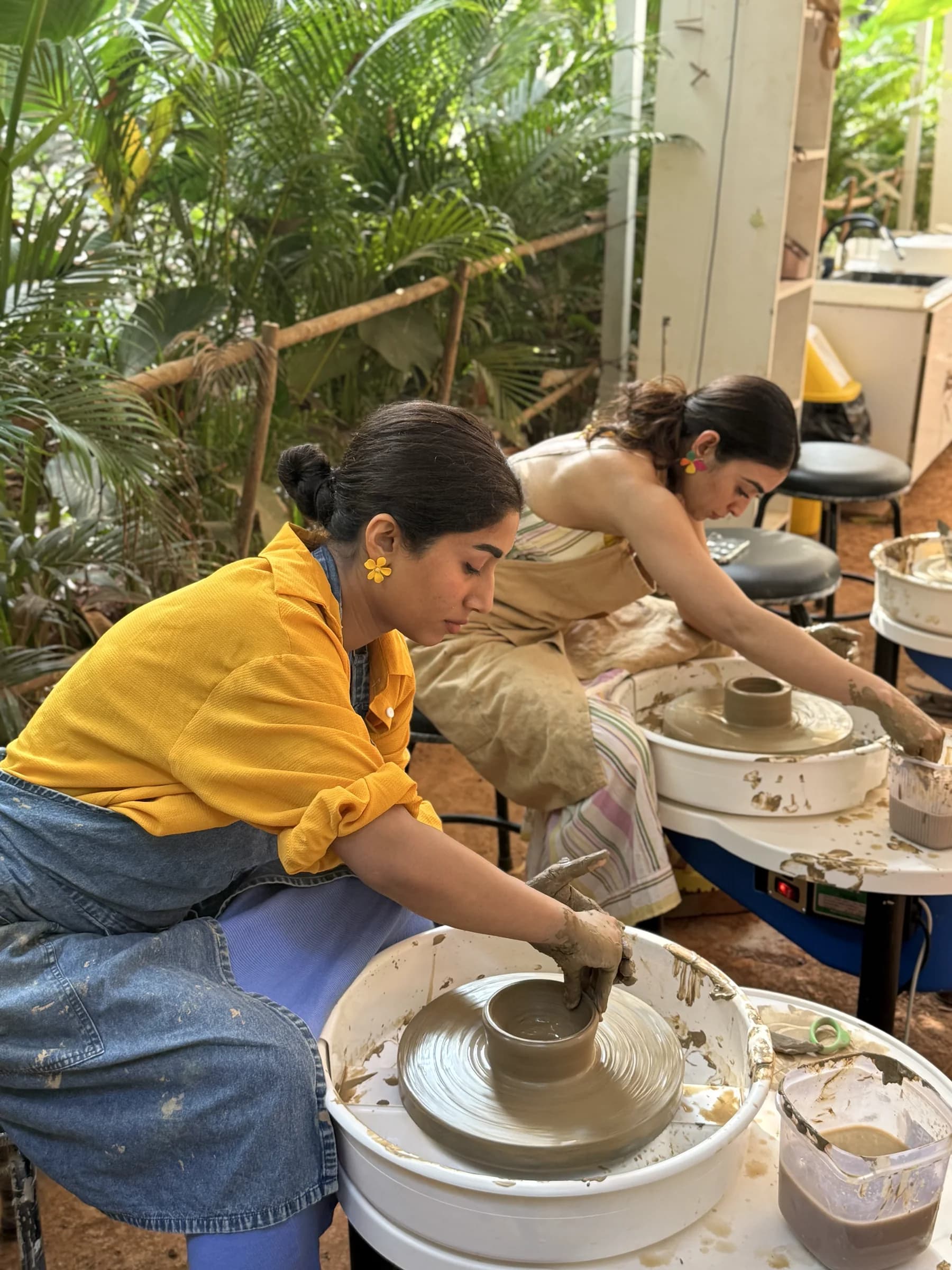 Two retreat participants leaning over pottery wheels as they shape clay bowls in the Goa studio.