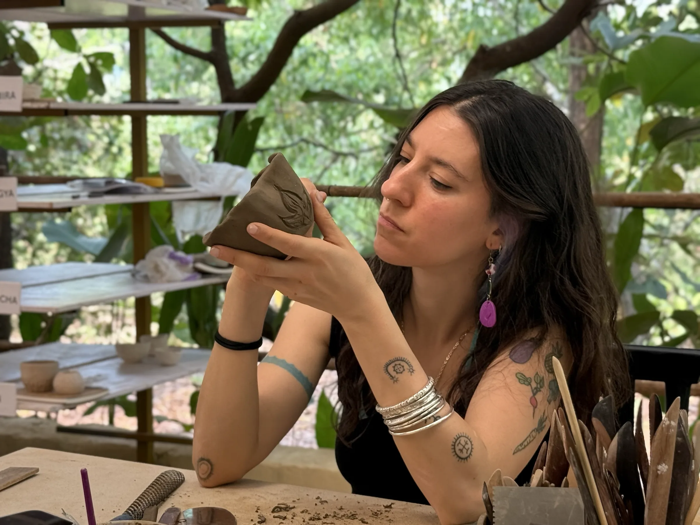 Participant lifting an in-progress clay form to inspect its profile and carved details in the Goa studio.