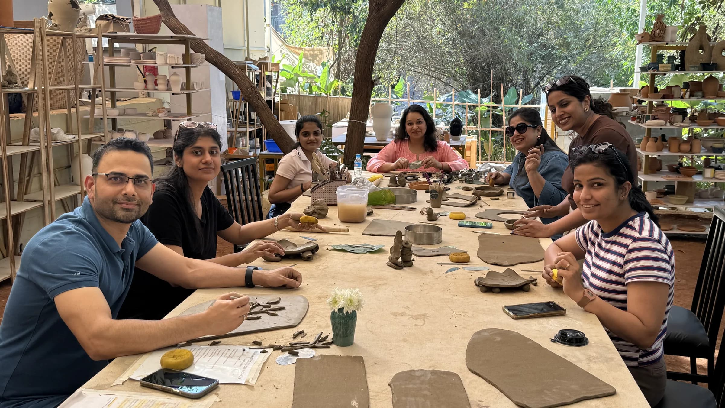 A full handbuilding workshop group seated around a clay-covered table at Dharamkot Studio in Goa.